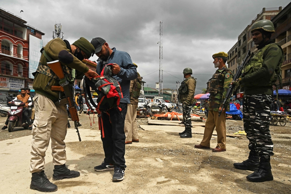 An Indian security personnel searches the bag of a pedestrian during a random search in Srinagar on April 20, 2023. (Photo by Tauseef Mustafa / AFP)