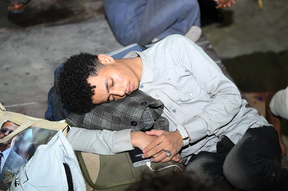 A man sleeps over a suitcase as people fleeing fighting across Sudan gather on April 26, 2023 in Port Sudan. (Photo by AFP)

