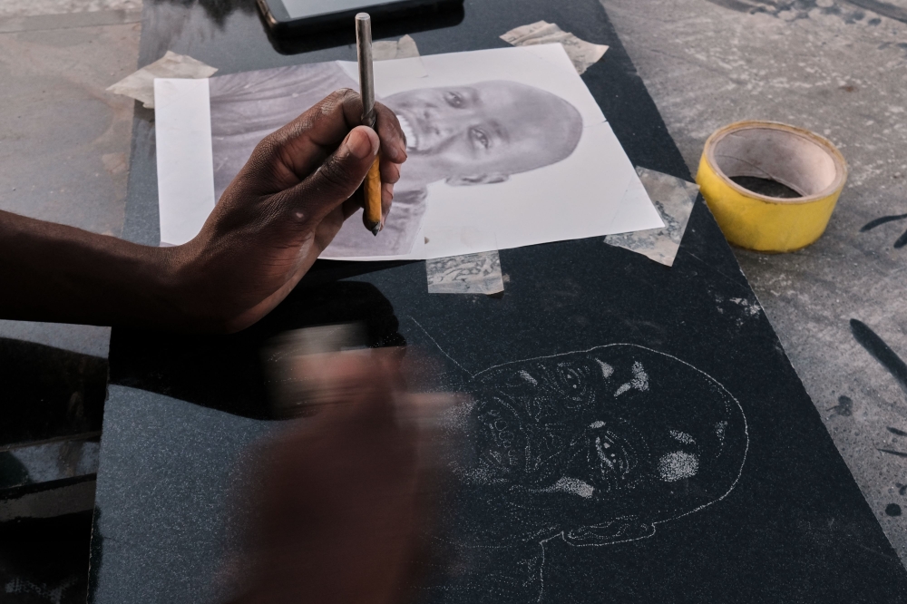 Denzel Karombe a 19-year-old school leaver who engraves portrait artworks onto polished black granite tombstones for Nyumba Yanga, a tombstone-making business uses a drill bit and tapping stone to etch a potrait at his workstation in Rugare township Harare, Zimbabwe April 21, 2023. Photo by Jekesai NJIKIZANA / AFP