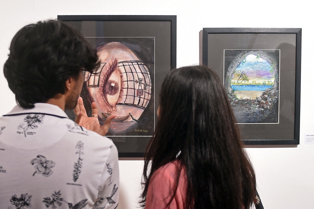 Visitors look at the paintings made by Ahmed Rabbani, during an exhibition of his work, in Karachi. (Photo by Rizwan Tabassum / AFP) 