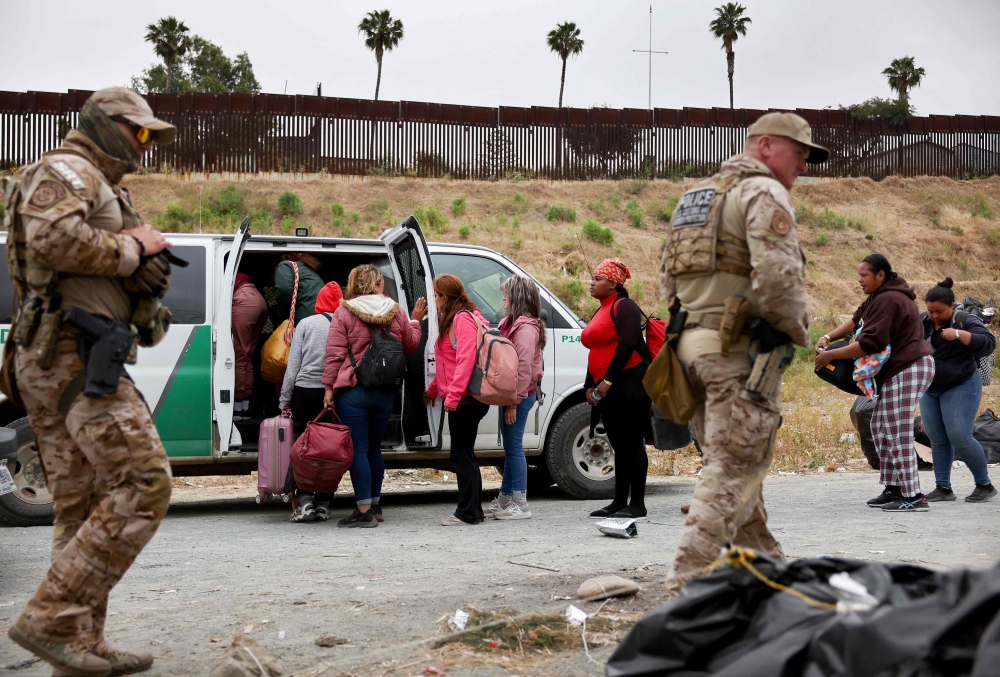 Customs and Border Protection officers walk as immigrants enter a vehicle to be transported from a makeshift camp between border walls, between the U.S. and Mexico, on May 13, 2023 in San Diego, California. (Photo by MARIO TAMA / GETTY IMAGES NORTH AMERICA / Getty Images via AFP)