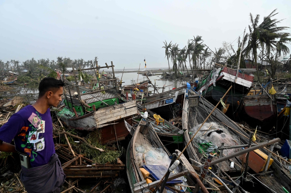 A local resident looks at broken boats in Sittwe, in Myanmar's Rakhine state, on May 15, 2023, after cyclone Mocha made a landfall. (Photo by Sai Aung Main / AFP)