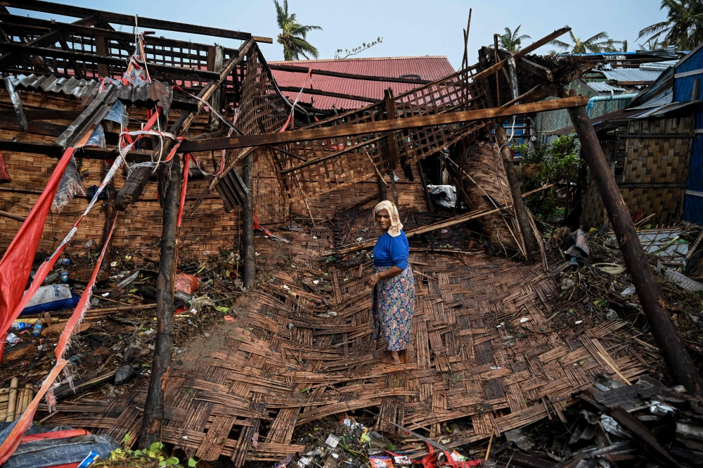 A Rohingya woman stands in her destroyed house at Basara refugee camp in Sittwe on May 16, 2023. (Photo by SAI Aung MAIN / AFP)