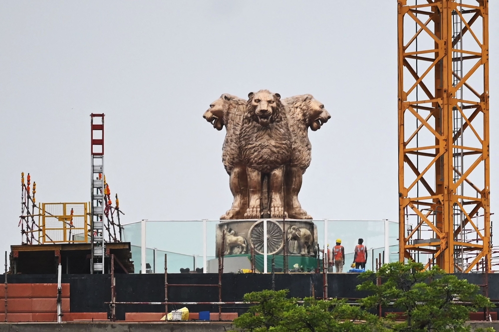 In this file photo taken on July 12, 2022, workers stand next to the newly inaugurated 'National Emblem' installed on the roof of the new Indian parliament building in New Delhi. (Photo by Sajjad Hussain / AFP)