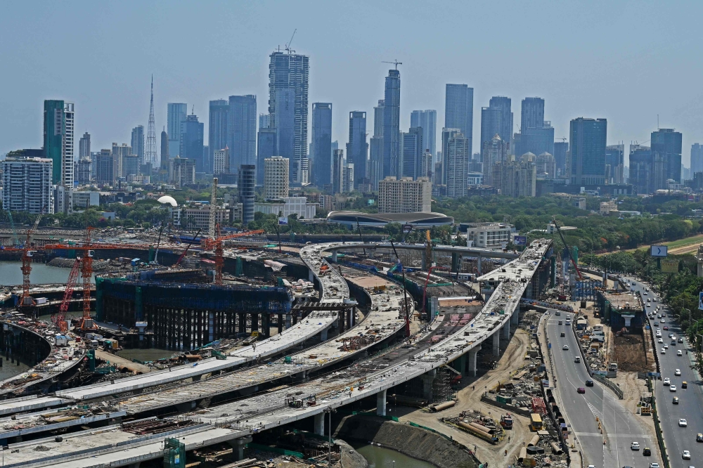 The city skyline is seen beside a construction site of a coastal road project near Haji Ali mosque in Mumbai on May 31, 2023. (Photo by Punit Paranjpe / AFP)