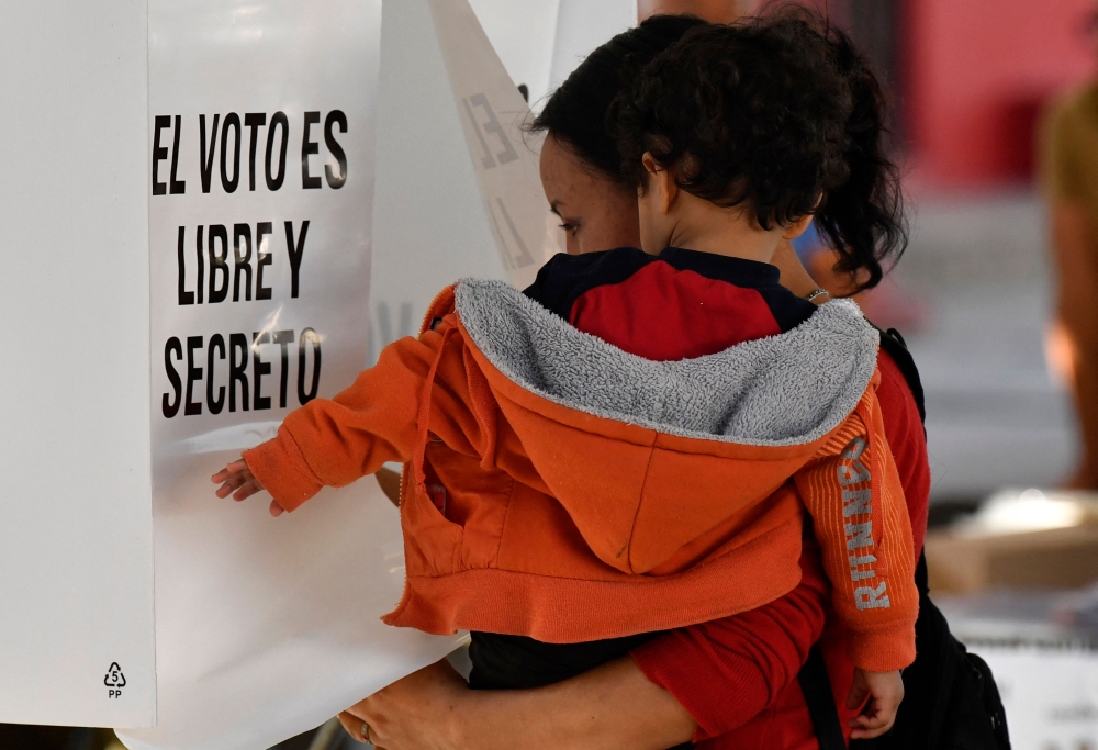 A woman carrying a child casts her ballot at a polling station in Texcoco, Mexico, on June 4, 2023, during gubernatorial elections in the State of Mexico. (Photo by CLAUDIO CRUZ / AFP)