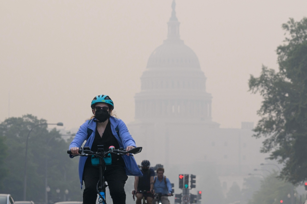 A cyclist rides under a blanket of haze partially obscuring the US Capitol in Washington, DC, on June 8, 2023. (Photo by Mandel Ngan / AFP)