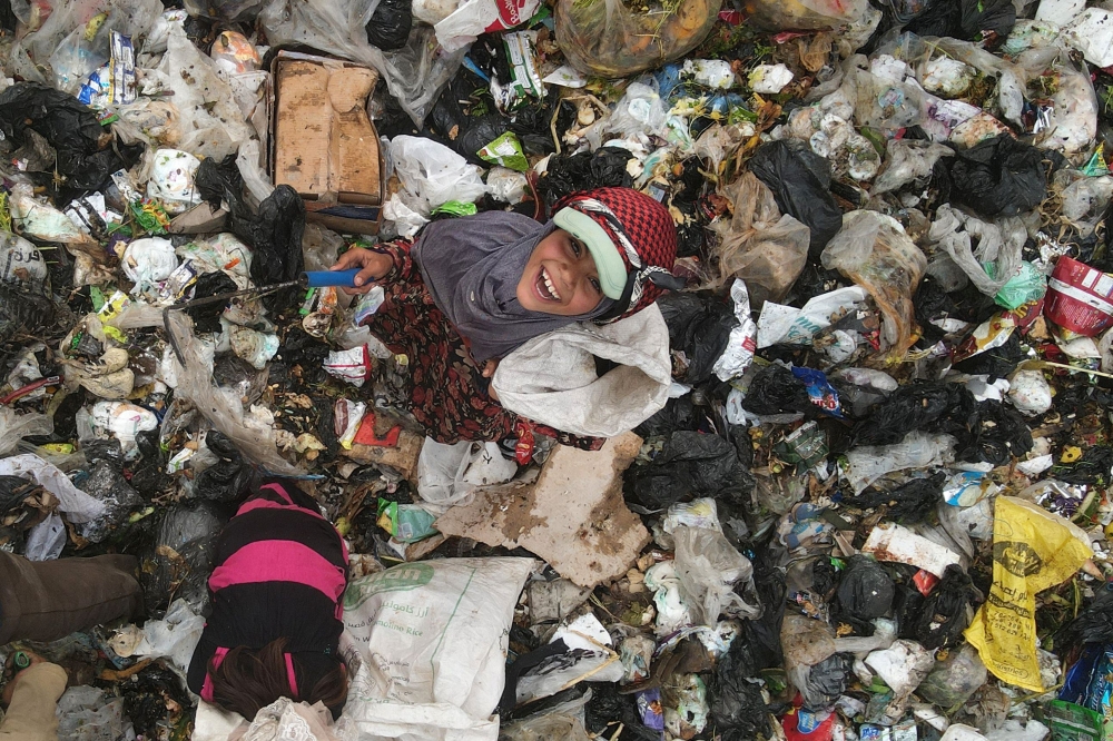 In this aerial view taken on June 3, 2023, a child smiles as she sifts through the rubbish with a scythe, looking for plastic items to sell for recycling, at a dump site near the village of Hazreh in Syria's northwestern Idlib province. (Photo by Aaref Watad / AFP)