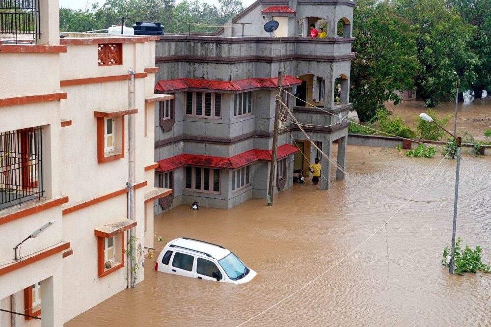 Residents watch as a car drowns in an inundated street at the coastal town of Mandvi as cyclone Biparjoy makes landfall on June 16, 2023. (Photo by AFP)