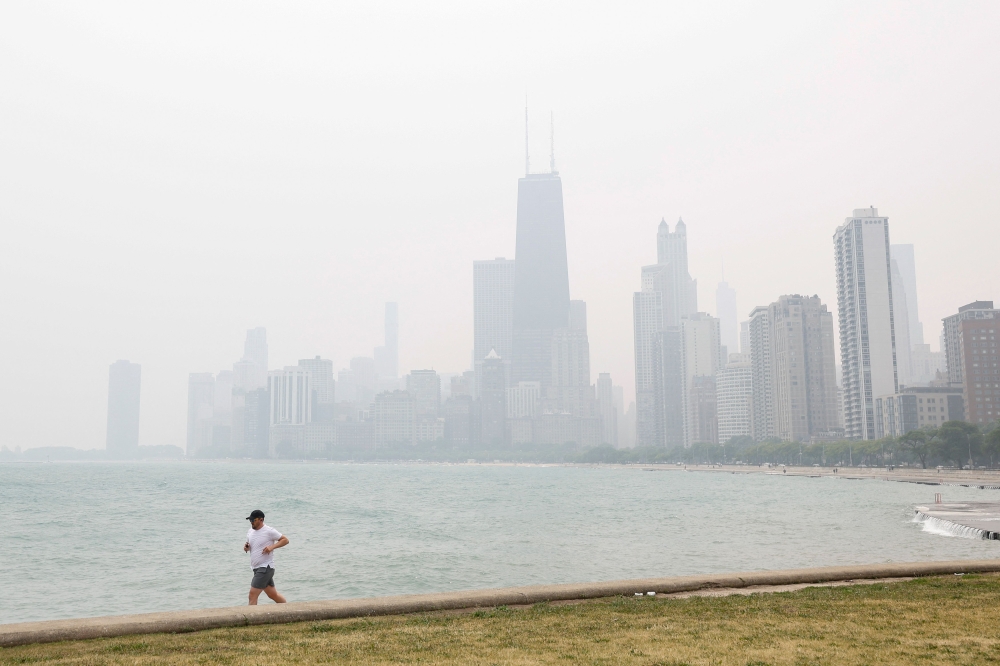 A jogger runs along the shoreline of Lake Michigan with heavy smoke from the Canadian wildfires in the background, on June 27, 2023, in Chicago, Illinois. (Photo by KAMIL KRZACZYNSKI / AFP)