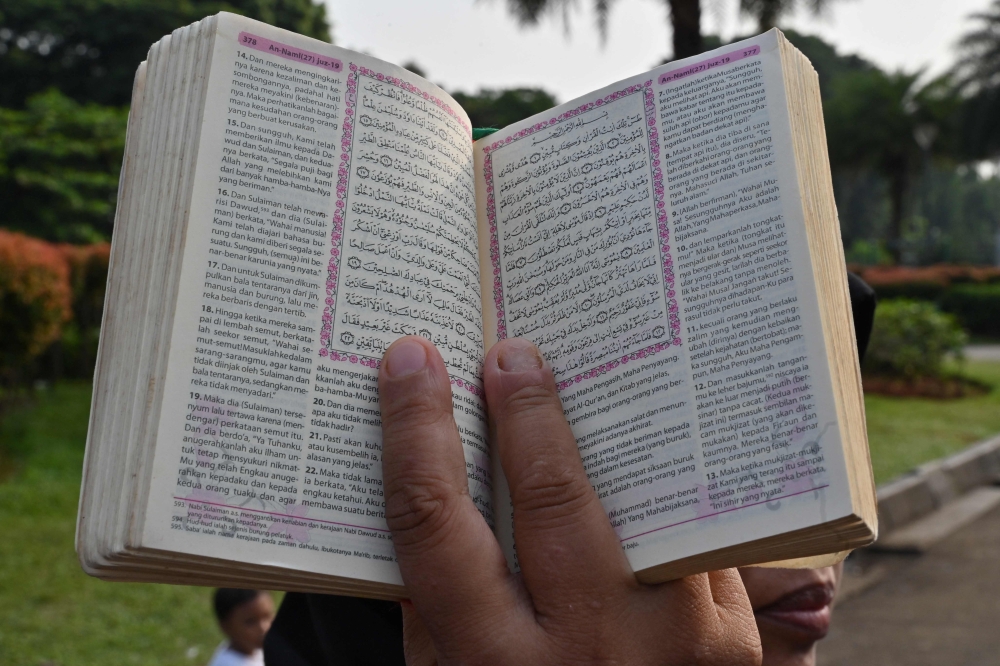 A demonstrator holds a copy of the Holy Quran with accompanying translation during a rally in Jakarta on July 2, 2023, as they protest against the burning of the Islamic holy book outside a Stockholm mosque that outraged Muslims around the world. (Photo by Adek Berry / AFP)