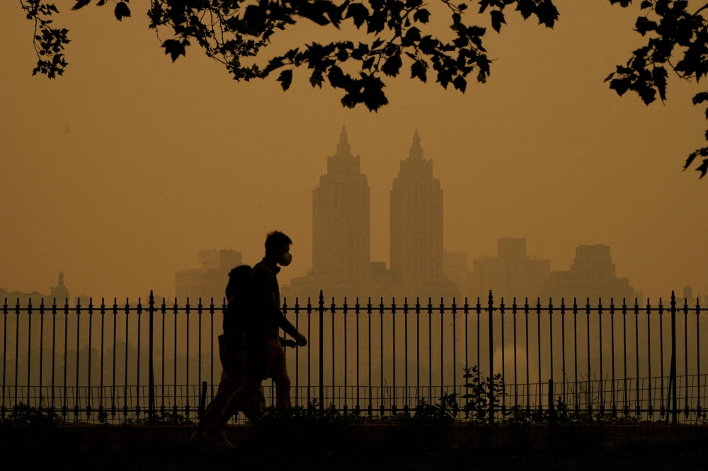 People walk in Central Park as smoke from wildfires in Canada cause hazy conditions in New York City on June 7, 2023. (Photo by Timothy A Clary / AFP)
