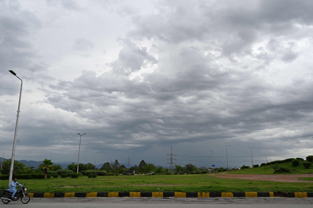 A motorcyclist rides past as dark clouds hover over Islamabad on July 7, 2023. (Photo by Aamir QURESHI / AFP)
