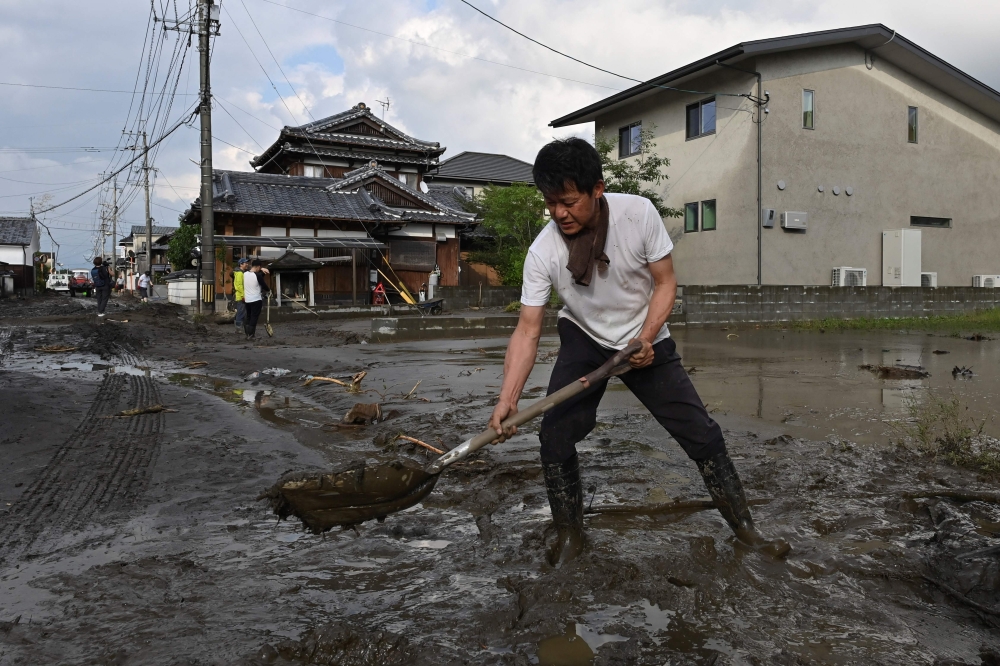 A man clears silt from a road following flooding in the city of Kurume, Fukuoka prefecture, on July 10, 2023, after heavy rains hit wide areas of Kyushu island. (Photo by Kazuhiro NOGI / AFP)

