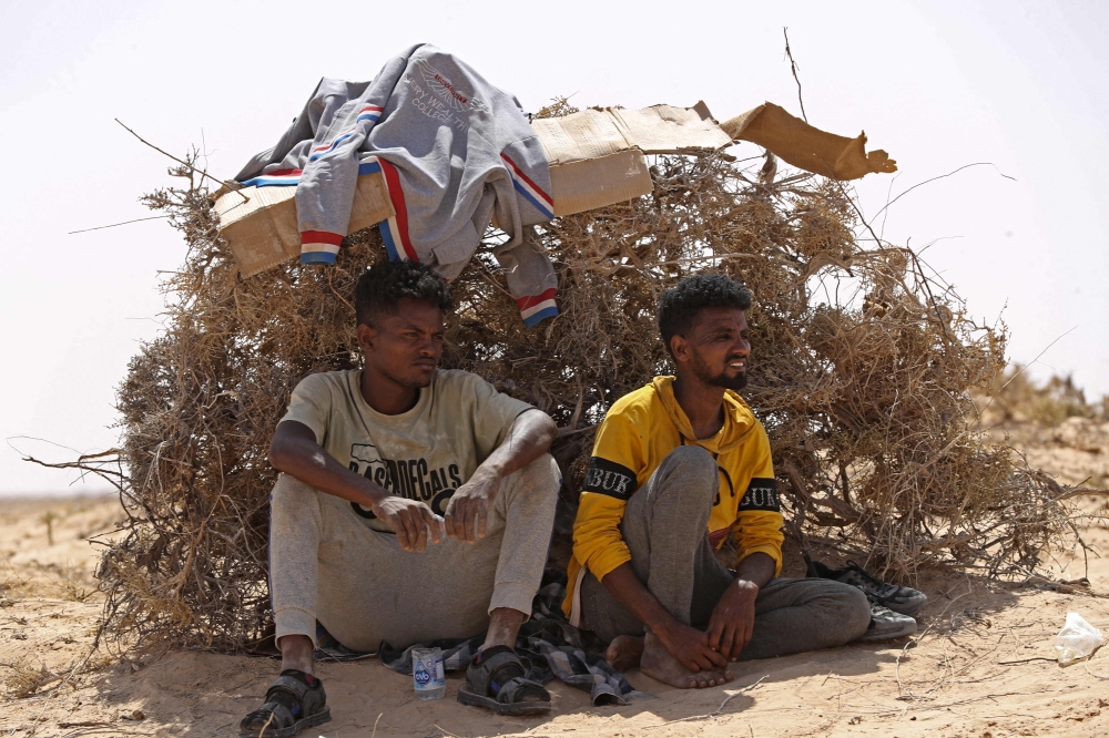 Migrants from sub-Saharan African countries who claim to have been abandoned in the desert by Tunisian authorities, shield themselves from the scorching summer heat in an uninhabited area near the border town of Al-Assah on July 16, 2023. (Photo by Mahmud Turkia / AFP)
