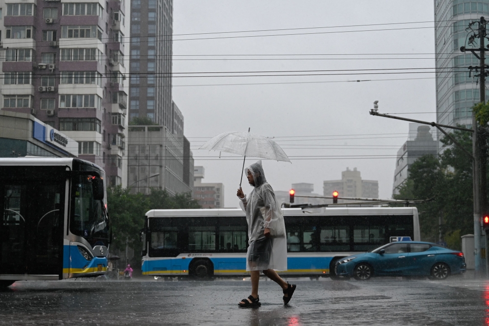 A man shelters from the rain with an umbrella in Beijing on July 31, 2023. (Photo by Pedro Pardo / AFP)