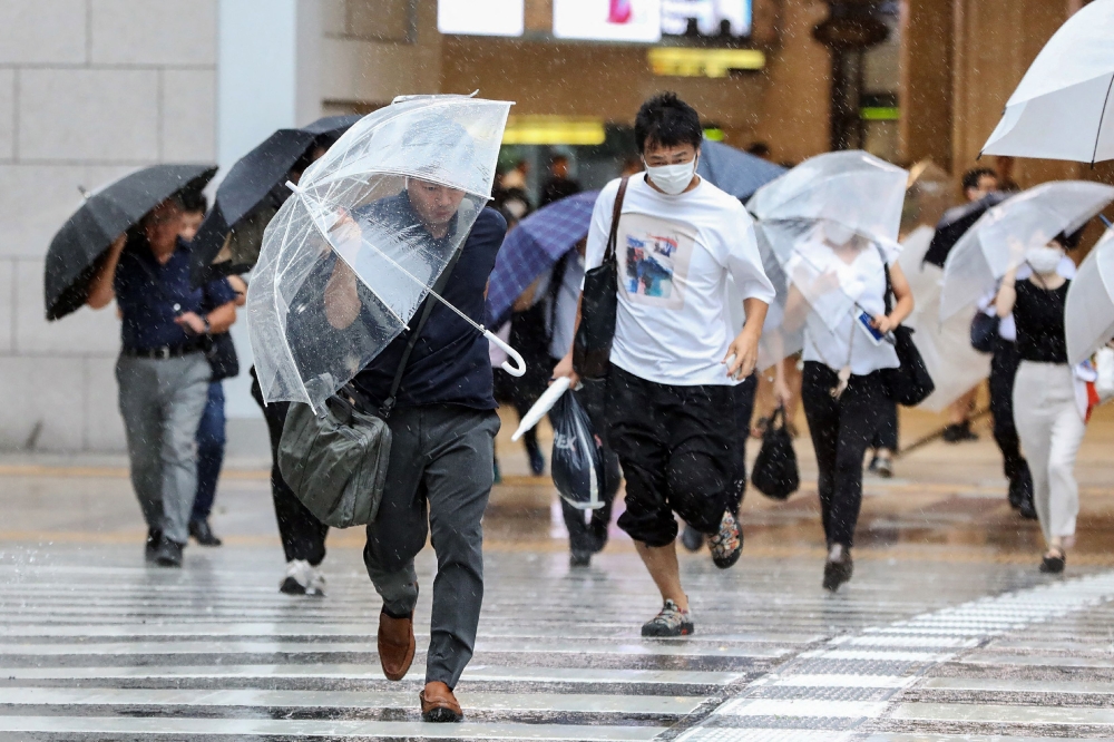 Pedestrians try to shield from wind and rain as they cross the street in front of Osaka Station on August 15, 2023, as Tropical Storm Lan hit the main island of Honshu overnight. Photo by JIJI Press / AFP