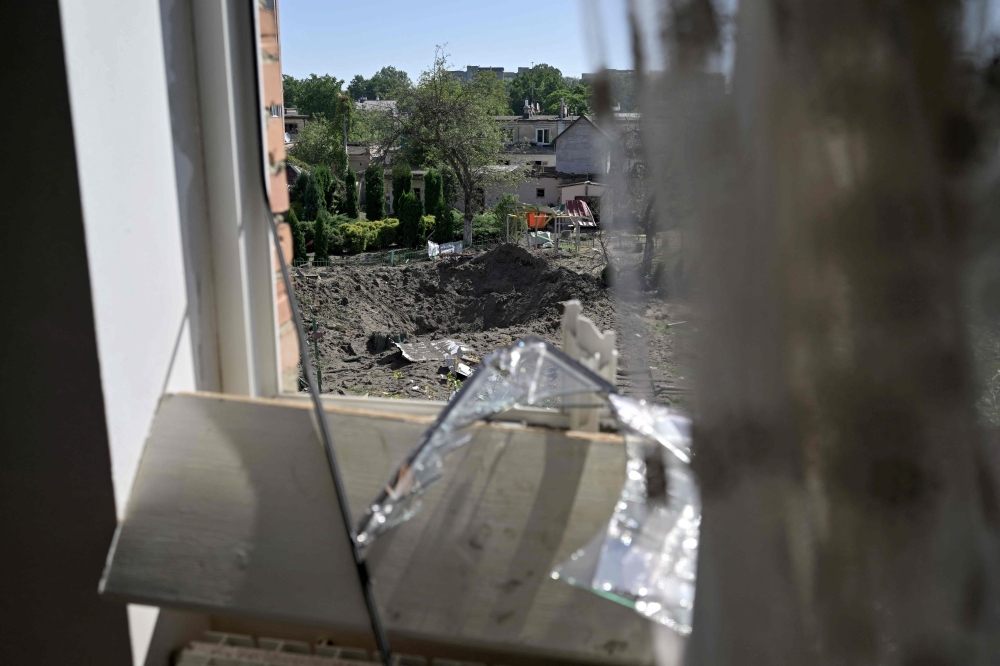 A view taken through a shattered window pane shows the crater of a missile that fell between residential buildings and a kindergarten in the city of Lviv, western Ukraine, on August 15, 2023, amid Russian invasion in Ukraine. Photo by Genya SAVILOV / AFP