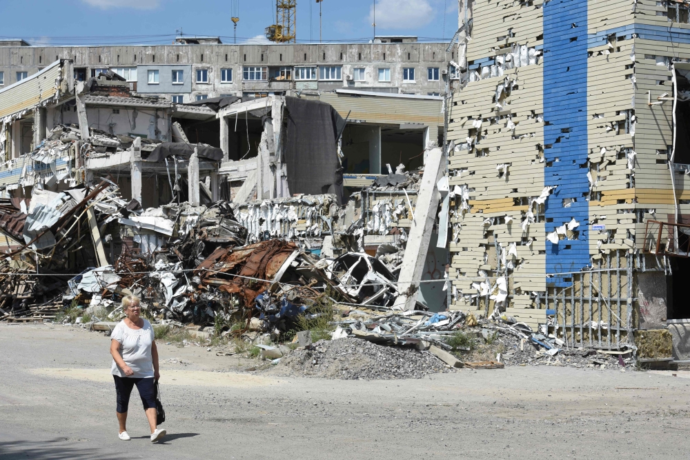 A woman walks past a destroyed building in Mariupol on August 16, 2023, amid the Russian invasion of Ukraine. (Photo by Stringer / AFP)