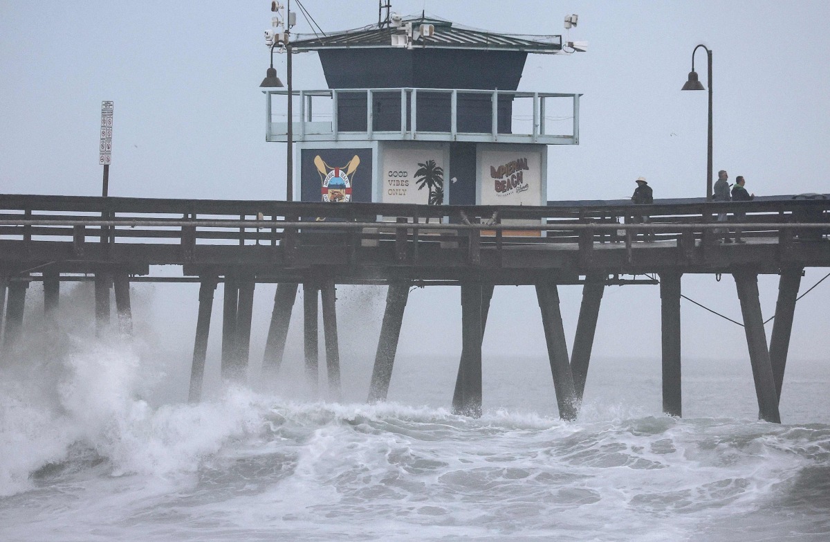People stand on a pier over the Pacific Ocean with Tropical Storm Hilary approaching in San Diego County on August 20, 2023 in Imperial Beach, California. (Photo by Mario Tama/ AFP)