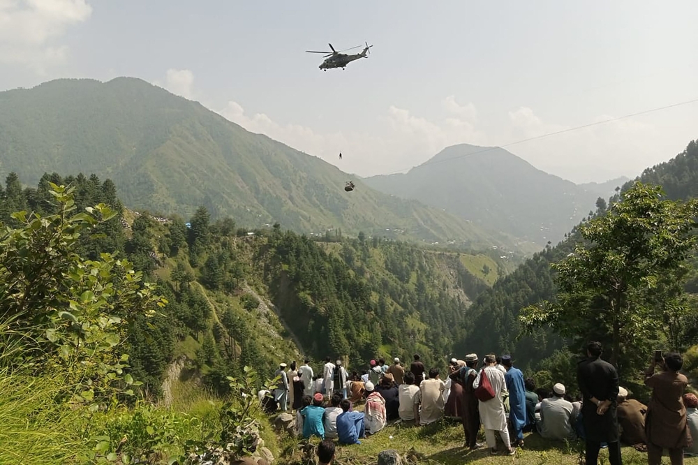 People watch as an army soldier slings down from a helicopter during a rescue mission to recover students stuck in a chairlift in Pashto village of mountainous Khyber Pakhtunkhwa province, on August 22, 2023. (Photo by AFP) 