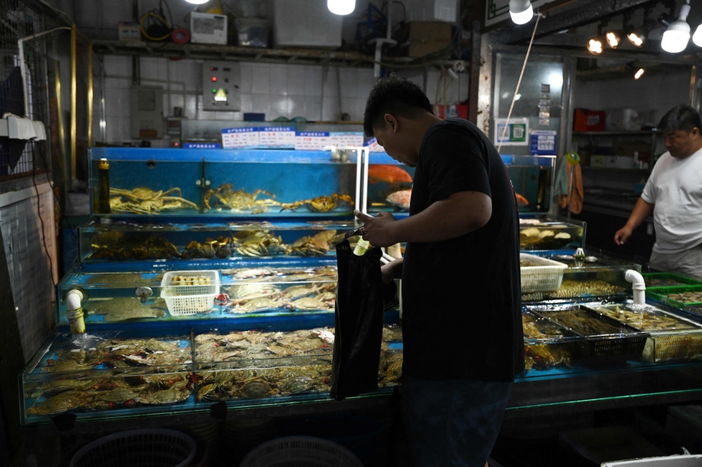A vendor collects seafood at a wholesale fish market in Beijing on August 24, 2023. (Photo by Greg Baker / AFP)
