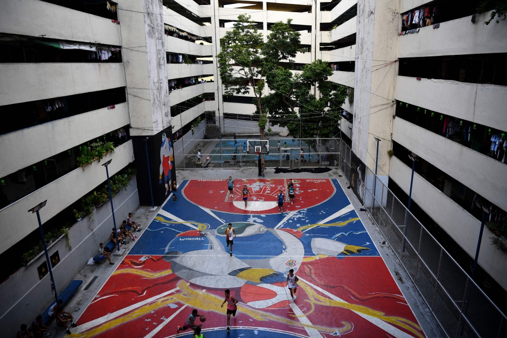 This photo taken on August 19, 2023 shows residents playing basketball on a court decorated with the FIBA World Cup 2023 logo, at a public housing project in Taguig city, suburban Manila. (Photo by Ted Aljibe / AFP)