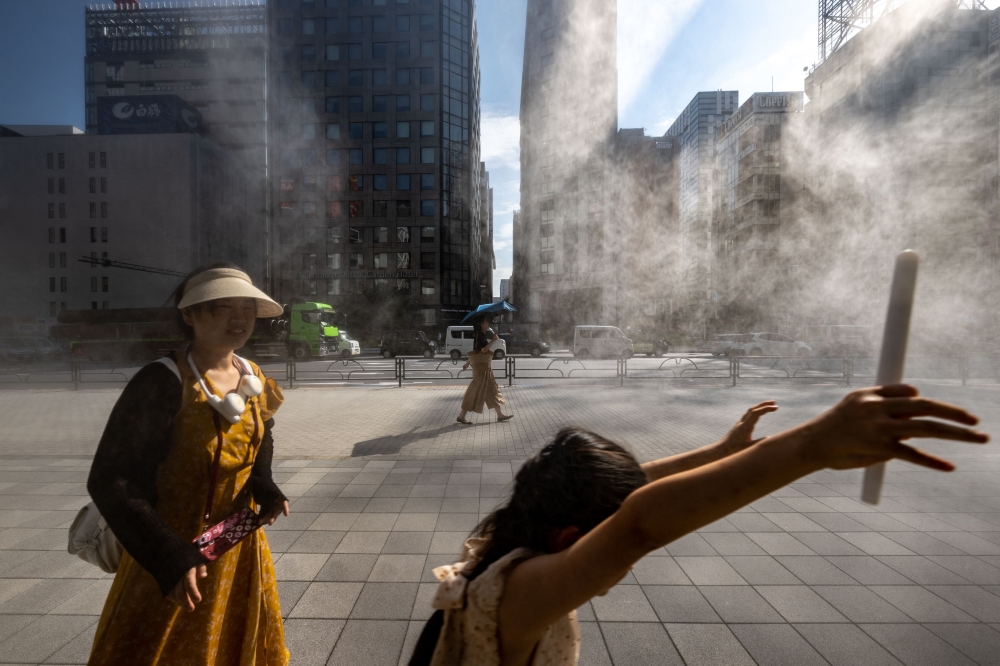 People walk past an overhead water misting system on a hot day in the Ginza district of Tokyo on July 10, 2023.(Photo by Philip Fong / AFP)