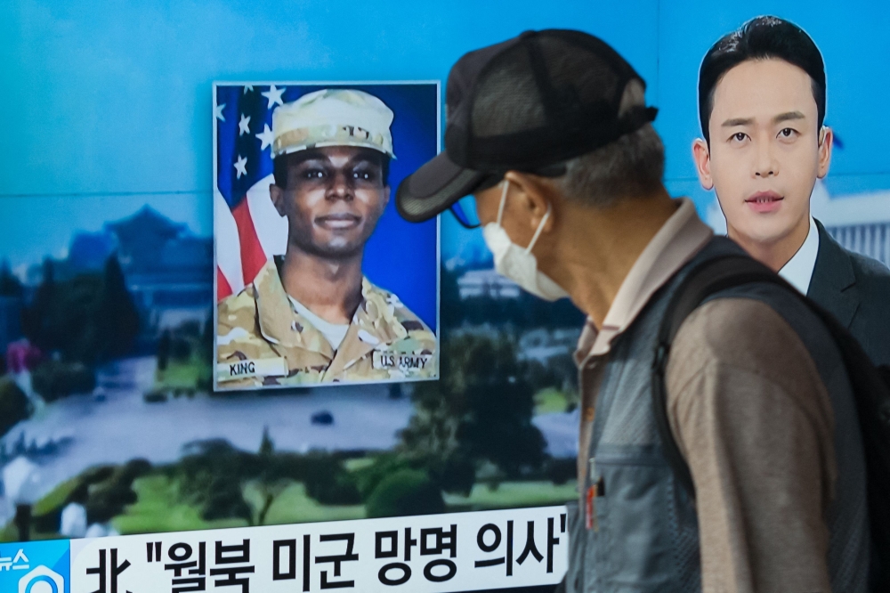 In this photo taken in Seoul on August 16, 2023, a man walks past a television showing a news broadcast featuring a photo of US soldier Travis King (C), who ran across the border into North Korea while part of a tour group visiting the Demilitarized Zone on South Korea's border on July 18. (Photo by Anthony WALLACE / AFP)

