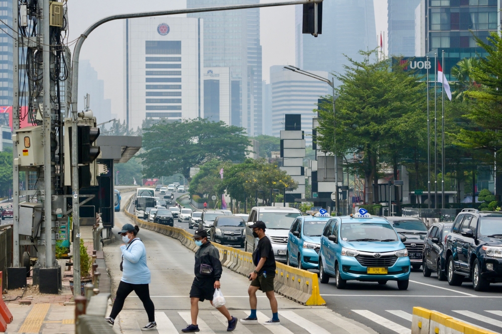 People cross a street on a polluted day in Jakarta on October 1, 2023. Photo by BAY ISMOYO / AFP
