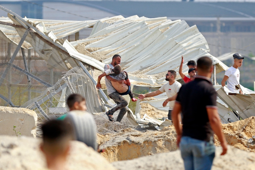 A man carries away a Palestinian killed in an Israeli airstrike at the Erez crossing between Israel and the northern Gaza Strip, on October 7, 2023. (Photo by Bashar Taleb / AFP)