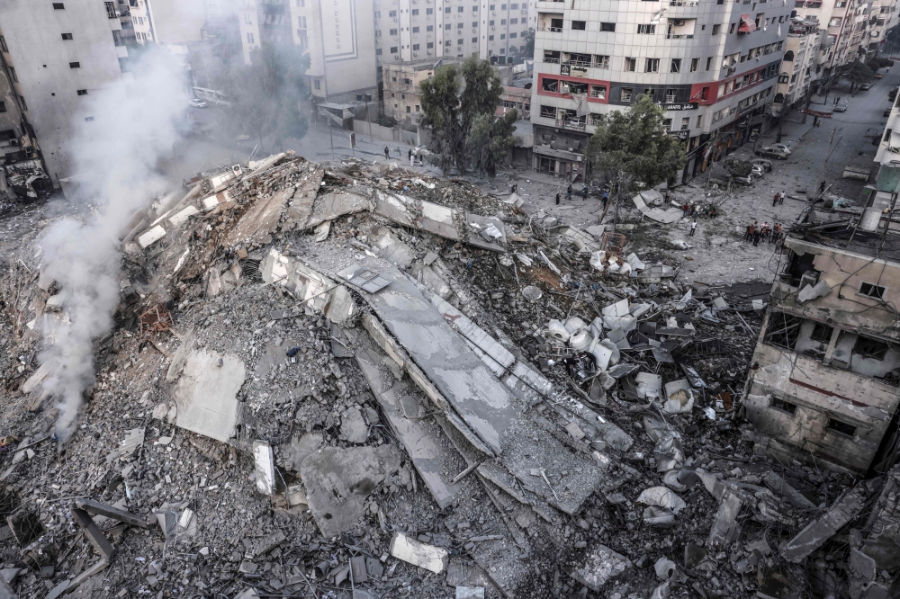 People walk around the ruins of a building destroyed in Israeli airstrikes in Gaza City on October 8, 2023. (Photo by Mohammed Abed / AFP)