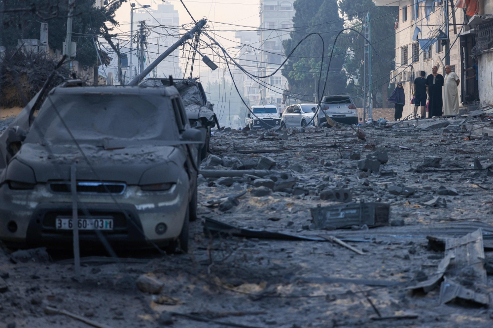 People walk past ruins on a street impacted by Israeli airstrikes in Gaza City on October 8, 2023. Photo by MAHMUD HAMS / AFP