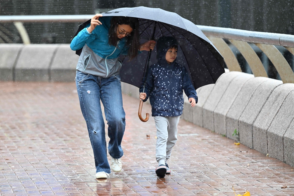 A woman and a child struggle with strong winds as Hong Kong hoisted typhoon signal no 8 around noon on October 8, 2023 as typhoon Koinu skirted by after the financial hub was affected again by a super typhoon and historic rainstorm last month. Photo by Peter PARKS / AFP