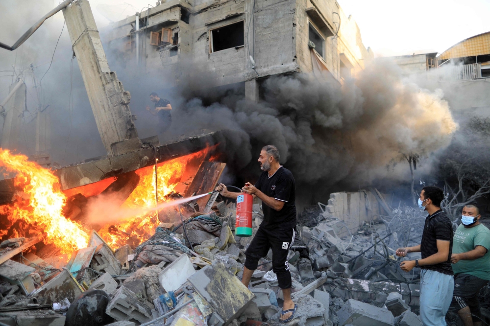 A Palestinian man uses a fire extinguisher to douse a fire following an Israeli strike, in Khan Yunis in the southern Gaza Strip on October 14, 2023. (Photo by Yasser Qudih / AFP)