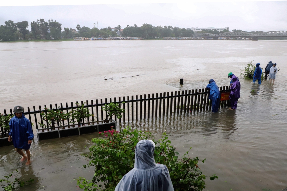 This photo taken on October 13, 2023 shows local workers removing fallen trees on a flooded road by the Perfume River in Hue city in central Vietnam. (Photo by Tam GIANG / AFP)