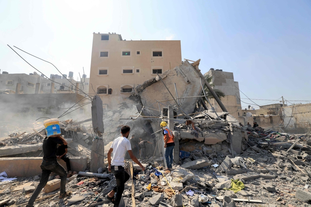 Palestinians survey the rubble of a collapsed building following an Israeli strike, in Khan Yunis in the southern Gaza Strip on October 14, 2023, amid the ongoing battles between Israel and the Palestinian Islamist group Hamas. Photo by Mahmud Hams/ AFP