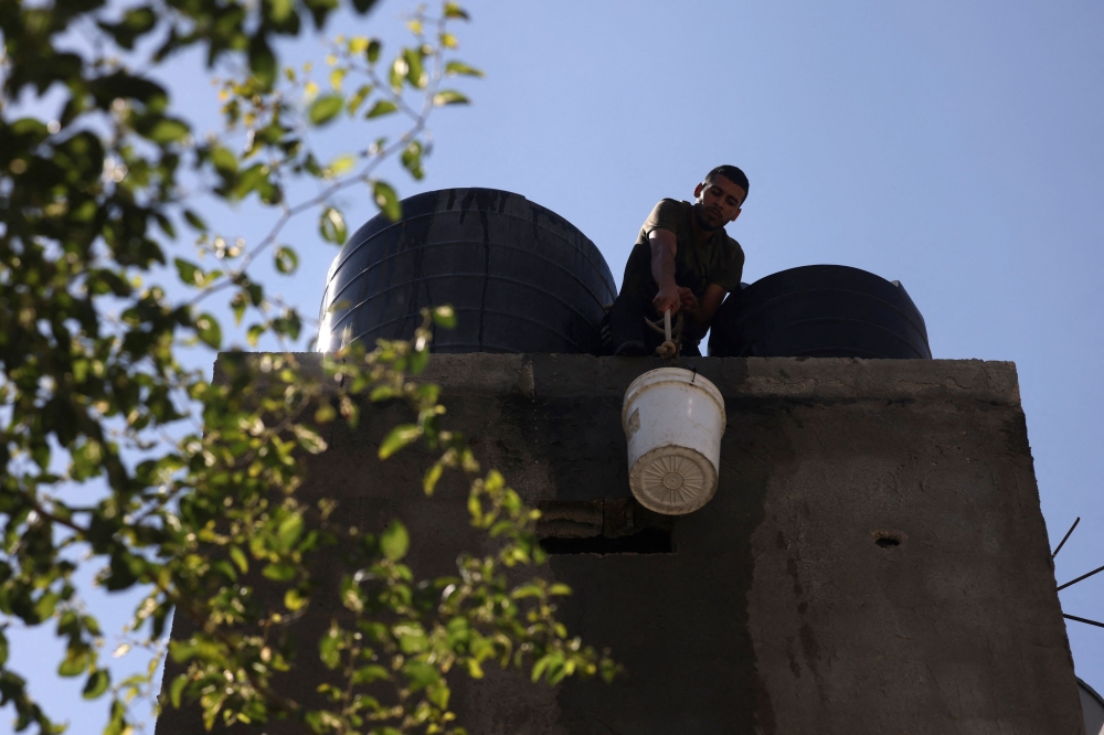 A man lifts a water bucket to the roof to refill a the water tank in a house in the Rafah refugee camp, in the southern of Gaza Strip on Octobers 15, 2023. (Photo by Mohammed Abed / AFP)