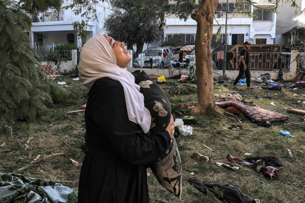 A woman reacts while holding a pillow as she stands amidst debris outside the site of the Ahli Arab hospital in central Gaza on October 18, 2023 in the aftermath of an overnight blast there. (Photo by Mahmud Hams / AFP)