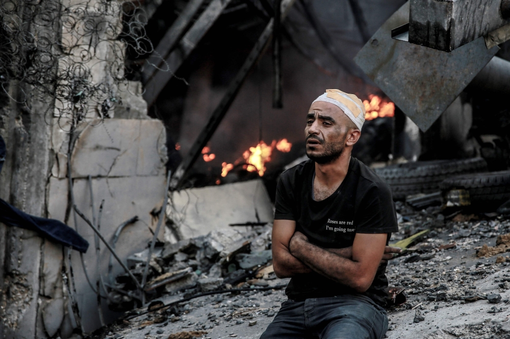 An injured man sits in front of a smouldering building in the aftermath of an Israeli strike on Gaza City on October 26, 2023, as battles continue between Israel and the Palestinian Hamas group. Photo by Omar El-Qattaa / AFP