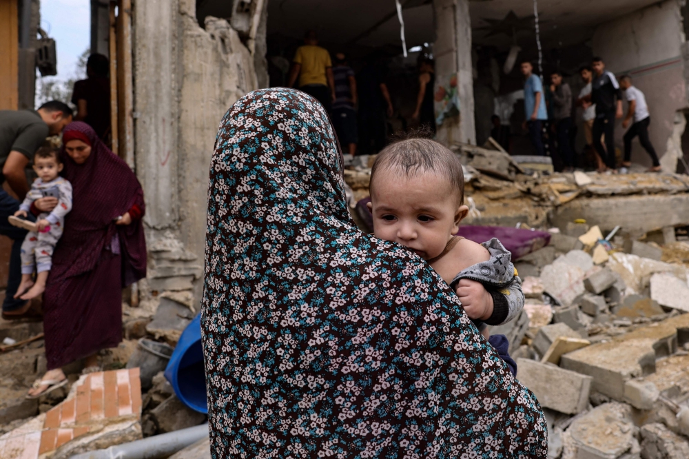 Women carry children as others check the damage in the aftermath of Israeli bombing in Rafah in the southern Gaza Strip on October 29, 2023. (Photo by Mohammed Abed / AFP)