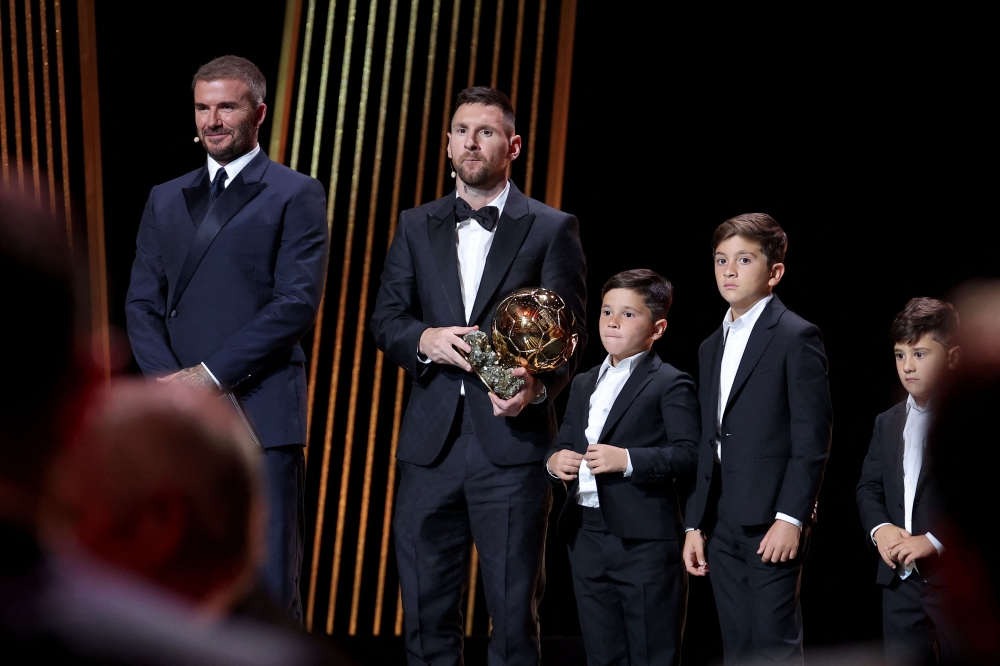 Lionel Messi (C) reacts with his trophy next to his children on stage as he receives his 8th Ballon d'Or award next to Former English football player and Inter Miami's co-owner David Beckham (L). (Photo by Franck Fife / AFP)