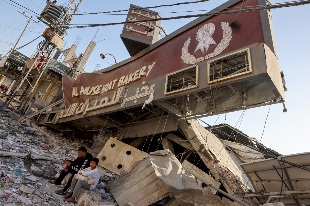 A Palestinian man and his son sit holding a bag of bread outside a destroyed bakery at the Nuseirat refugee camp in the central Gaza Strip on November 4, 2023. Photo by MOHAMMED ABED / AFP