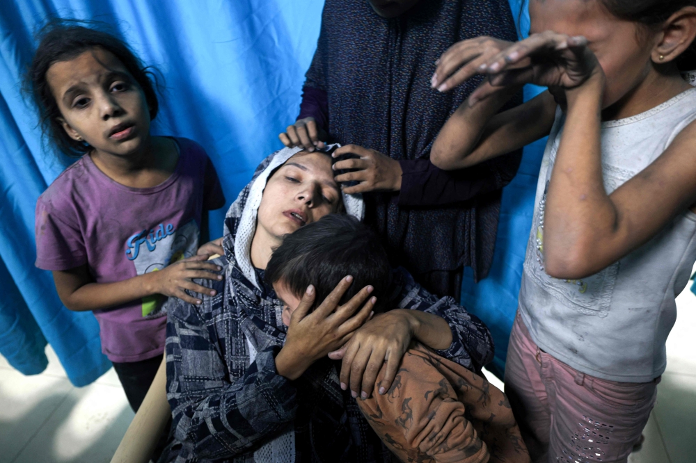 A wounded Palestinian woman from the Baraka family is surrounded by her children upon their arrival at Nasser Hospital in Khan Yunis in the southern Gaza Strip following Israeli air strikes that hit their building on November 13, 2023. Photo by Mahmud HAMS / AFP
