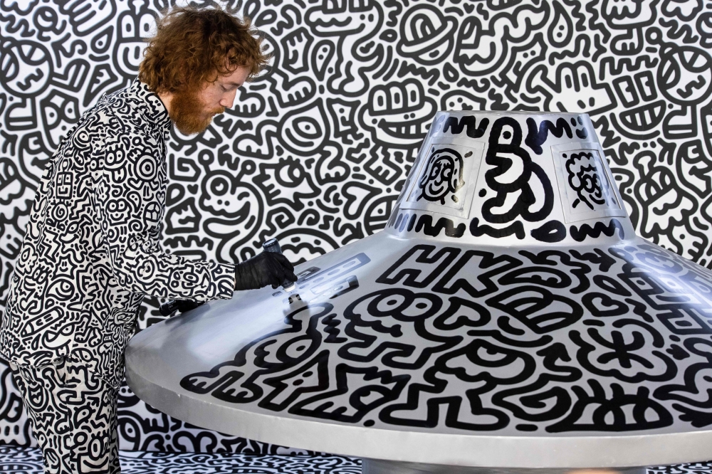 British artist Sam Cox, better known as Mr Doodle, draws on a model spaceship for a live art performance at Central MTR Station in Hong Kong on November 19, 2023. (Photo by Isaac Lawrence / AFP)