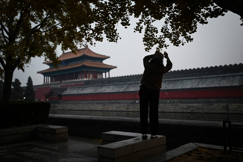 A woman takes a picture along the moat outside the Forbidden City in Beijing on November 21, 2023. Photo by WANG Zhao / AFP