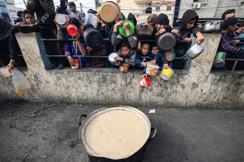 At a donation point in a refugee camp in in Rafah in the southern Gaza Strip, Palestinian men and children line up to collect food on December 23, 2023. Photos by Mahmud Hams / AFP
