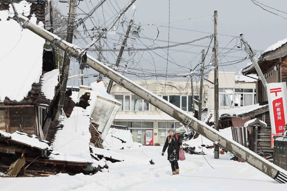 This photo taken on January 8, 2024 shows a woman walking under a downed utility pole after snow blanketed the disaster-hit area in the city of Suzu, Ishikawa prefecture, a week after a major 7.5 magnitude earthquake struck the Noto region in Ishikawa prefecture on New Year's Day. Photo by JIJI Press / AFP