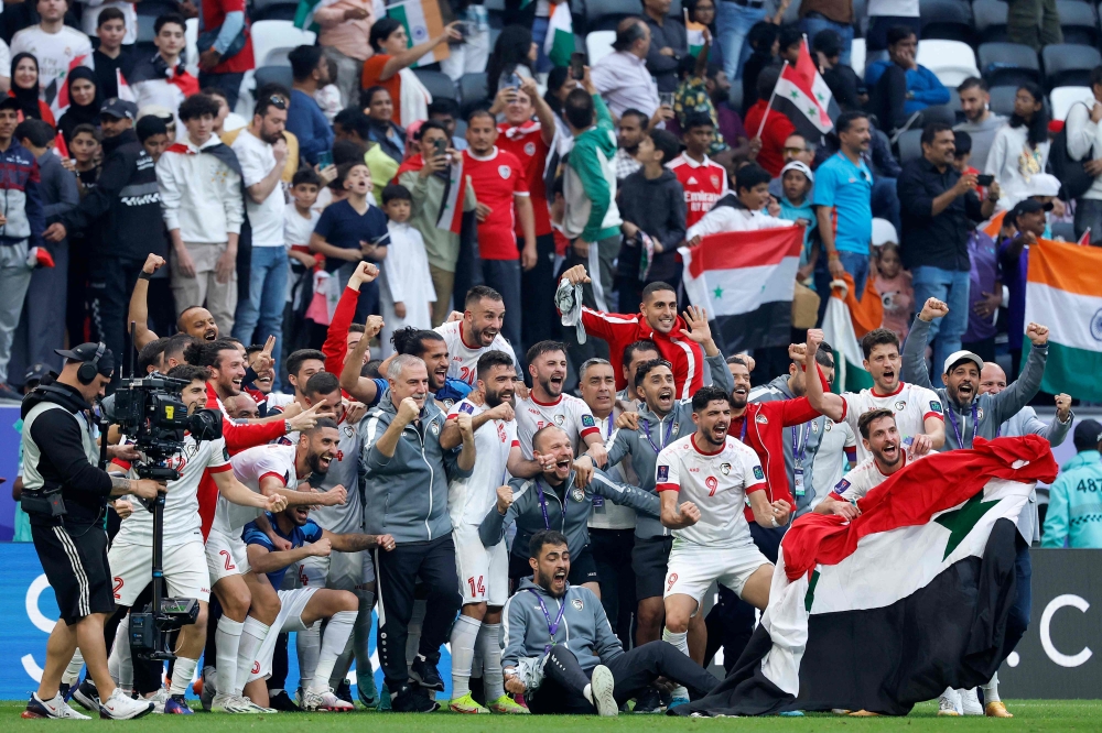 Syria's players celebrate with a national flag on the pitch after the Qatar 2023 AFC Asian Cup Group B football match between Syria and India at Al-Bayt Stadium in al-Khor, north of Doha, on January 23, 2024. (Photo by KARIM JAAFAR / AFP)