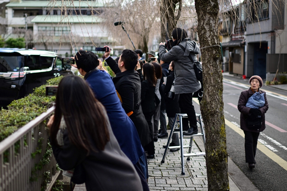 A woman (R) walks past as journalists (C) try to record the departure of a vehicle as it leaves the Kyoto District Court in Kyoto on January 25, 2024, following the verdict for a Japanese man who admitted to starting a fire that killed 36 people at an animation studio in 2019. Photo by Philip FONG / AFP